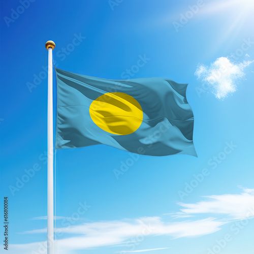 Waving flag of Palau on flagpole with sky background.
