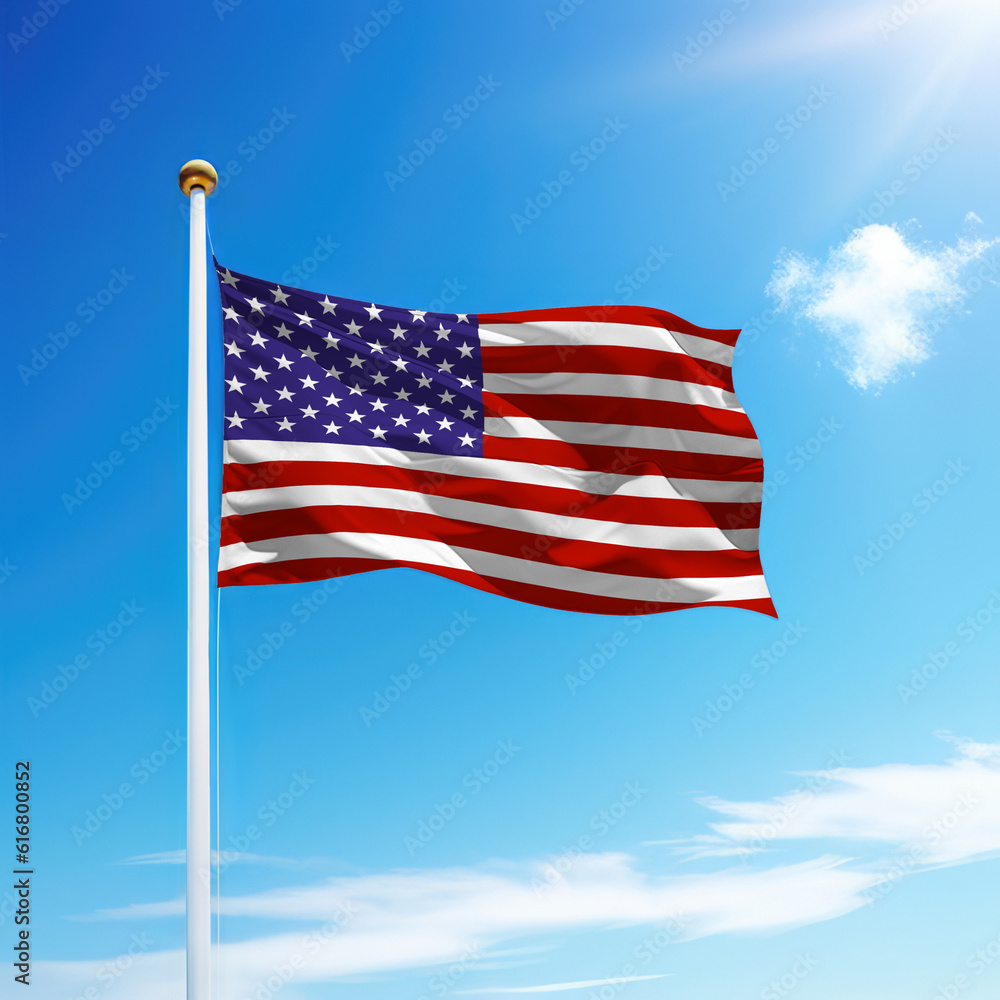 Waving flag of United States on flagpole with sky background.