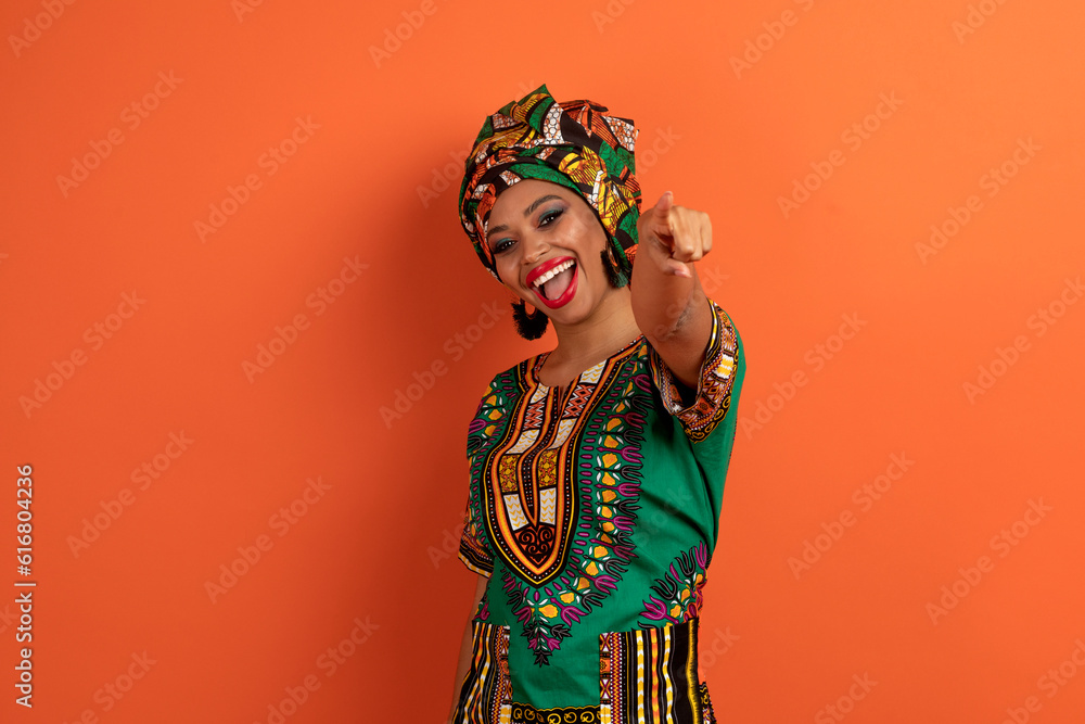 Positive cute black lady in african costume pointing at camera