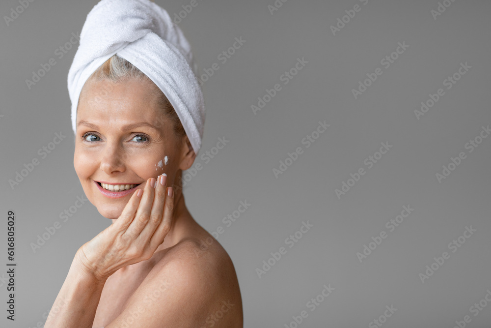 Spa and wellness concept. Attractive mature woman applying face cream after shower enjoying beauty and face care routine Spa and wellness concept. Attractive mature woman applying face cream after shower enjoying beauty and face care routine