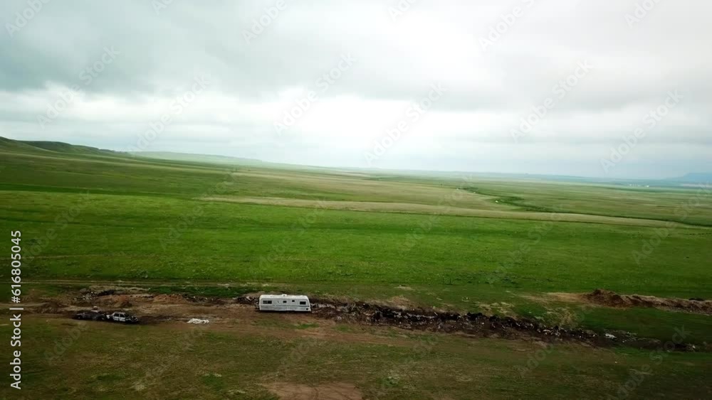 Aerial Panning Shot Of Abandoned Motor Home By Burnt Cars Against Sky, Drone Flying Over Green Landscape - Billings, Montana Aerial Panning Shot Of Abandoned Motor Home By Burnt Cars Against Sky, Drone Flying Over Green Landscape - Billings, Montana