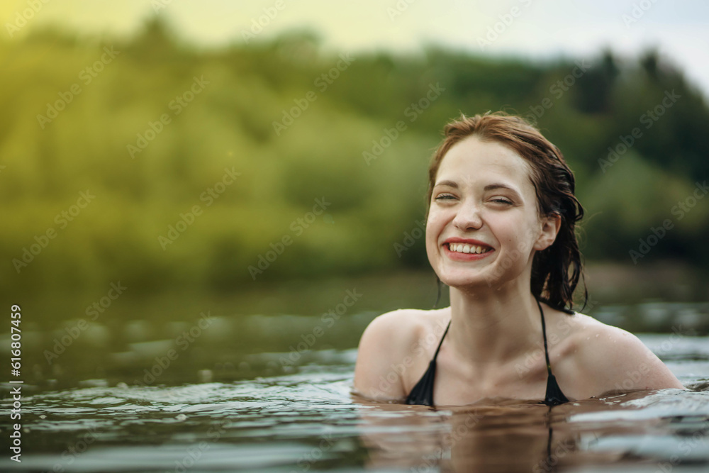 Fototapeta premium beautiful smiling woman bathes in the water of the lake, sea river. The concept of a happy vacation at sea.