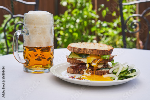 Variation on club sandwich consist from whithe bread, sunny side egg and melted beef with vegetables, served with mug of czech pilsner beer in the garden restaurant as a fresh, small and healthy lunch
