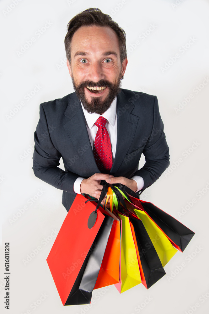 Bearded handsome man with shopping bags. 40s adult happy man wearing dark office suit holding shopping colored paper bags, boasting his purchases with huge discounts isolated on white background. Bearded handsome man with shopping bags. 40s adult happy man wearing dark office suit holding shopping colored paper bags, boasting his purchases with huge discounts isolated on white background.