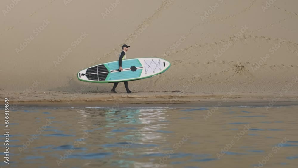 Man walking on shore with stand up paddle board along big dunes in desert. SUP Man walking on shore with stand up paddle board along big dunes in desert. SUP
