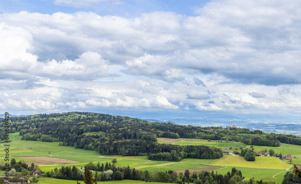 View of a forest, fields and village on the hills against a cloudy sky
