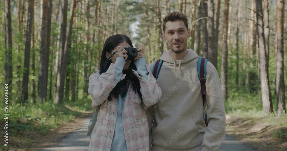 Happy couple walking in summer forest talking photo with camera and talking enjoying beautiful view. Photography and tourism concept. Happy couple walking in summer forest talking photo with camera and talking enjoying beautiful view. Photography and tourism concept.