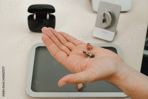 Modern miniature hearing aids. Small and discreet invisible hearing aids in hands. Closeup of patient. Hearing rehabilitation clinic 