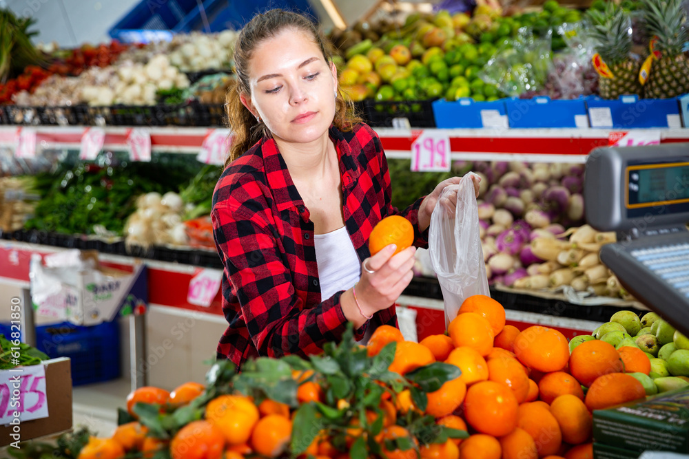 Positive european shopper chooses fresh oranges at grocery store