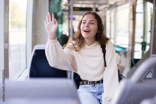 Young attractive woman sitting in tram near window and waving to people