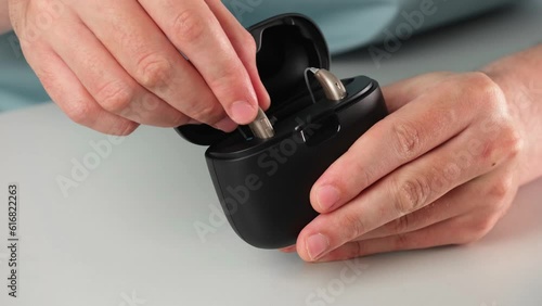 Patient charging hearing aid in special portable Smart Charger with built-in power bank. Case in man hands keeps hearing aids dry and safe