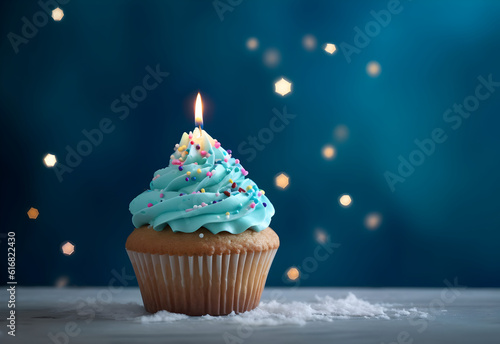 Birthday cupcake with a candle and festive tinsel decoration on a blue background with copy space. Generated AI. © AnaWein