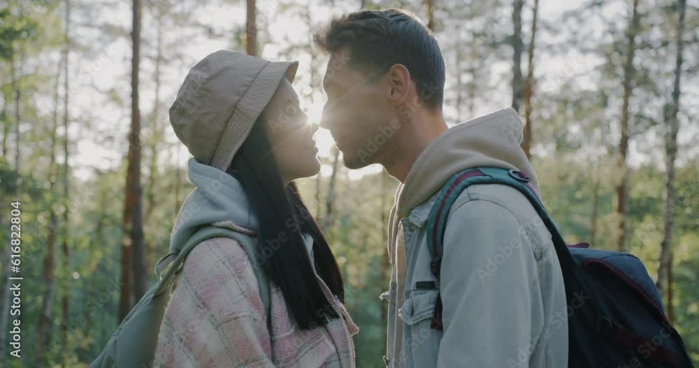 Slow motion of loving couple with backpacks expressing love touching faces standing in sunlit forest. Affection and relationship concept. Slow motion of loving couple with backpacks expressing love touching faces standing in sunlit forest. Affection and relationship concept.