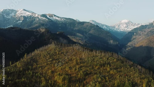Stunning view of mountain peaks covered with snow backlit with warm sunrise light, aerial drone shot of beautiful mountains and hills, spring season morning, mountain range golden hour