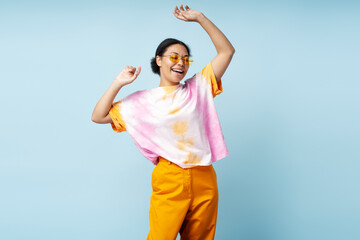 Portrait of beautiful happy African American woman dancing wearing trendy tie dye t shirt isolated on blue background. Smiling  stylish fashion model having fun posing for picture in studio 