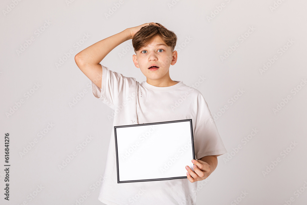 Shocked Teenage boy holding a blank sign isolated on white background. Banner. Young smiling boy show blank board. Close up male model portrait on white background. Shocked Teenage boy holding a blank sign isolated on white background. Banner. Young smiling boy show blank board. Close up male model portrait on white background.