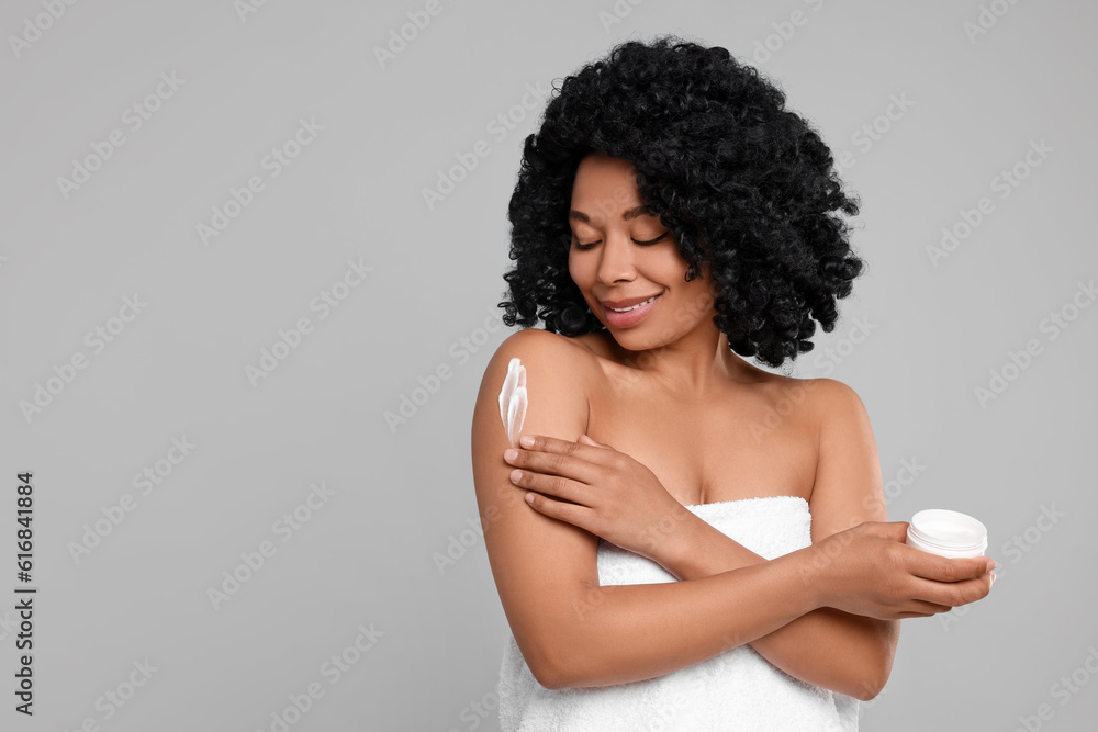 Young woman applying body cream onto shoulder on grey background. Space for text Young woman applying body cream onto shoulder on grey background. Space for text