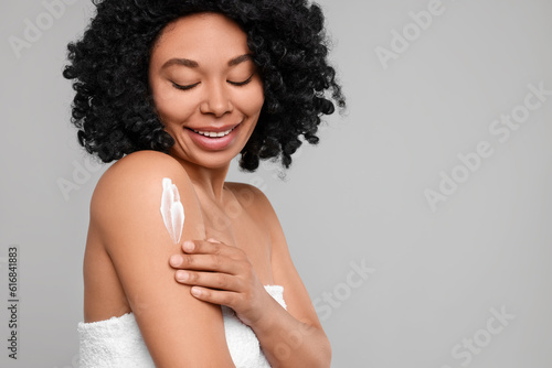 Young woman applying body cream onto shoulder on grey background. Space for text