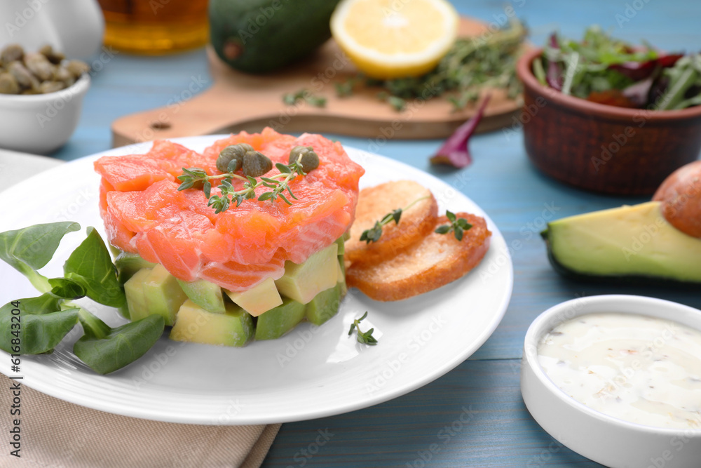 Delicious salmon tartare served with avocado and croutons on light blue table Delicious salmon tartare served with avocado and croutons on light blue table