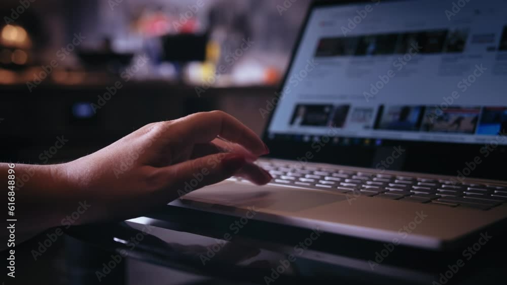 Connected Comfort: Close-Up of a Female Hand Surfing the Internet on a Laptop in a Cozy Evening Home Setting Connected Comfort: Close-Up of a Female Hand Surfing the Internet on a Laptop in a Cozy Evening Home Setting