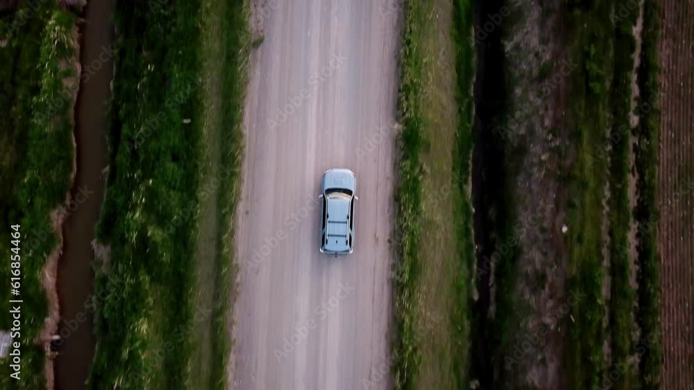 Aerial Tilt Up Shot Of Car On Dirt Road Amidst Green Plants, Drone Flying Forward Over Vehicle Against Sky - Billings, Montana Aerial Tilt Up Shot Of Car On Dirt Road Amidst Green Plants, Drone Flying Forward Over Vehicle Against Sky - Billings, Montana