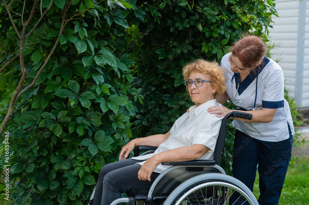 Caucasian female doctor walks with an elderly patient in a wheelchair in the park. Nurse accompanies an old woman on a walk outdoors. Caucasian female doctor walks with an elderly patient in a wheelchair in the park. Nurse accompanies an old woman on a walk outdoors.