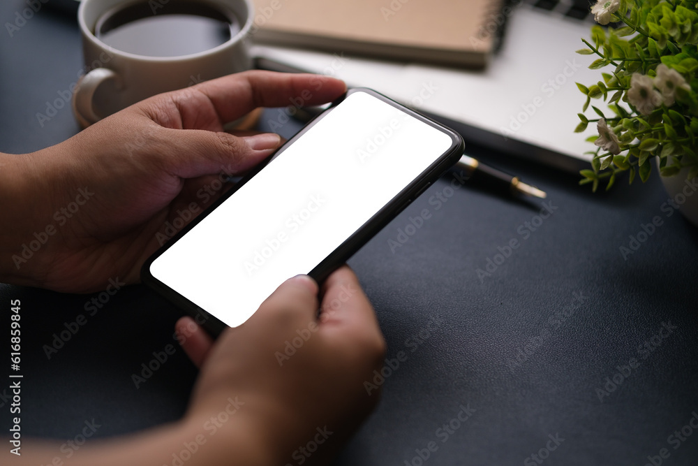 Over shoulder view of woman holding smart phone while sitting at her workspace. Over shoulder view of woman holding smart phone while sitting at her workspace.