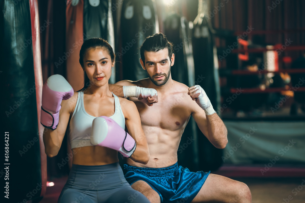 Asian woman training kick boxing with punching glove, fitness woman with physical exercising trainer by doing self defense workout or fitness activity in a wellness gym. Determined strong fighter Asian woman training kick boxing with punching glove, fitness woman with physical exercising trainer by doing self defense workout or fitness activity in a wellness gym. Determined strong fighter