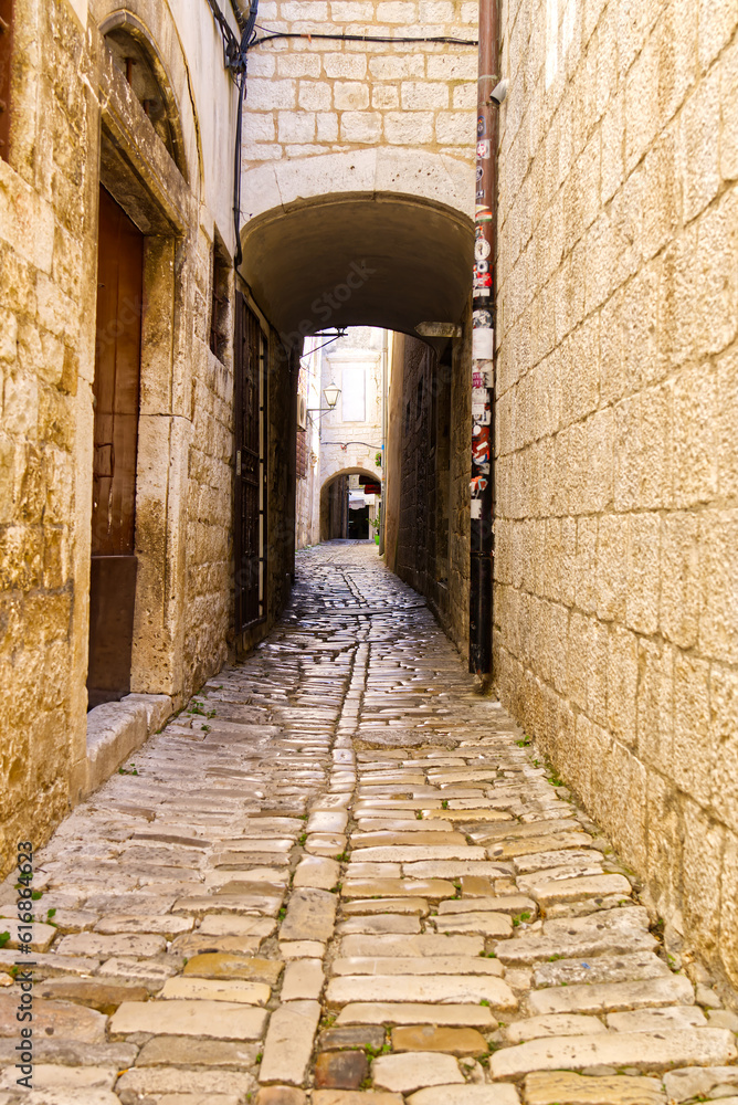 Obraz premium Narrow street with stone houses. Old houses and old narrow alley in Trogir, Croatia, Europe. Streets in old town.