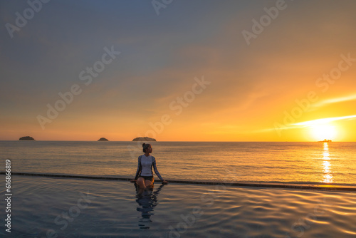Women relaxed in outdoor pool on sunset near the ocean. Summer travel vacation concept, relax in luxury infinity pool.