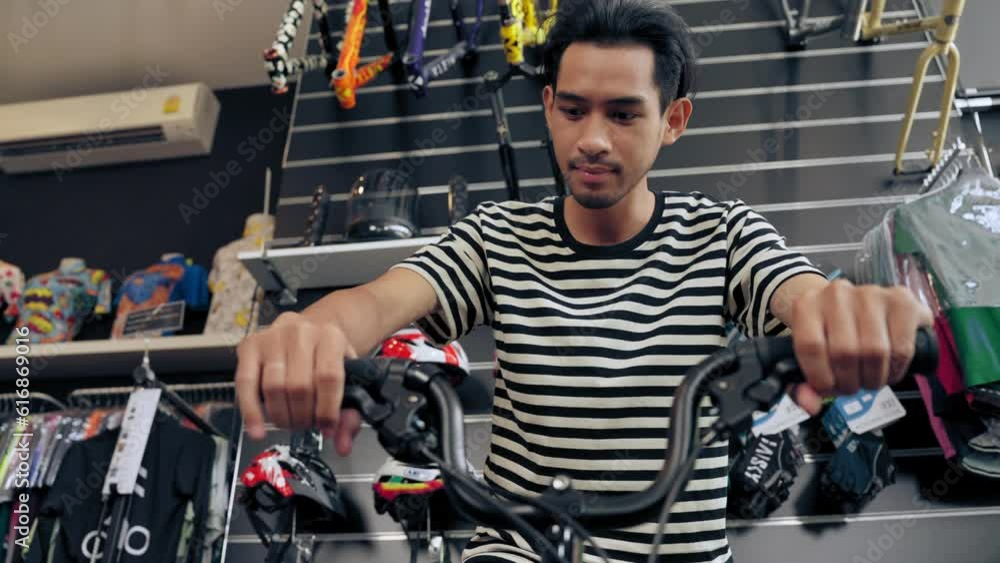 Young Asian man test riding and check handlebars and brake of bike before decide selection buy new bicycle in shop. Consumerism concept Young Asian man test riding and check handlebars and brake of bike before decide selection buy new bicycle in shop. Consumerism concept