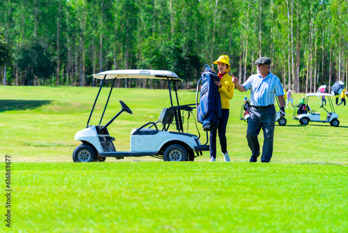 Φωτογραφία Asian senior man with female caddy driving golf cart together on golf course to fairway at country club