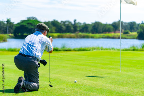 Asian senior man holding golf club hitting golf ball on fairway at country club in sunny day. Healthy retired elderly man golfer enjoy outdoor activity sport golfing at golf course on summer vacation
