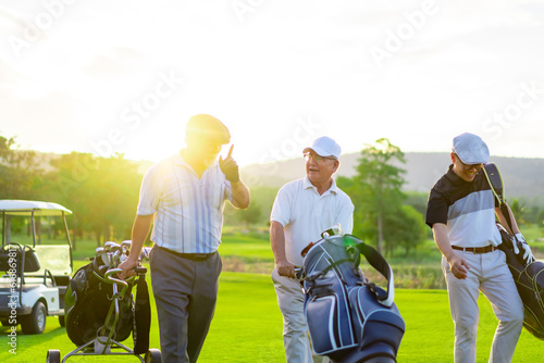 Group of Asian businessman and senior CEO holding golf bag walking on golf course with talking together. Healthy people enjoy outdoor sport lifestyle golfing at country club on summer holiday vacation