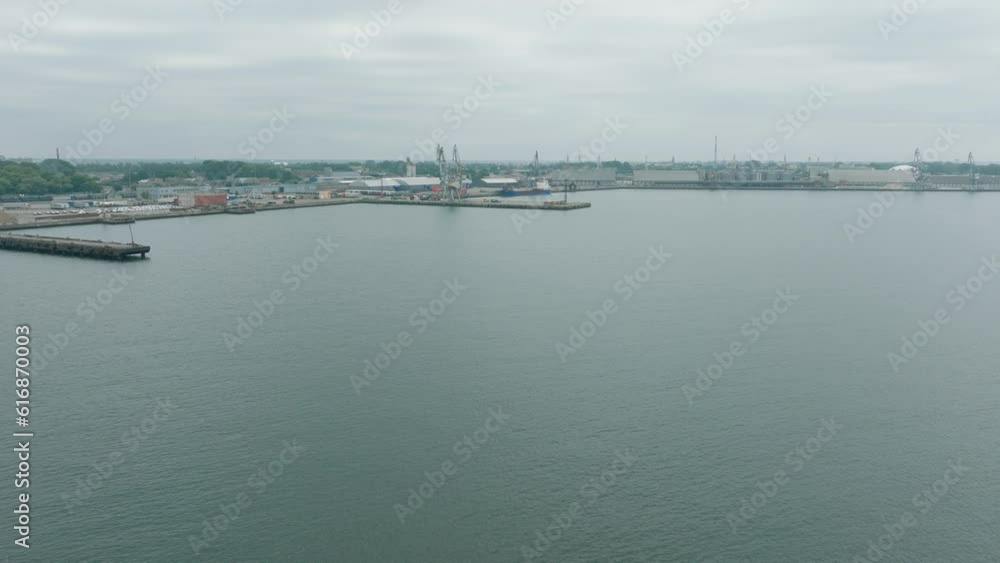 Aerial establishing view of port cranes and empty loading docks at Port Of Liepaja (Latvia), Liepaja city in the background, overcast summer day, wide drone shot moving forward Aerial establishing view of port cranes and empty loading docks at Port Of Liepaja (Latvia), Liepaja city in the background, overcast summer day, wide drone shot moving forward