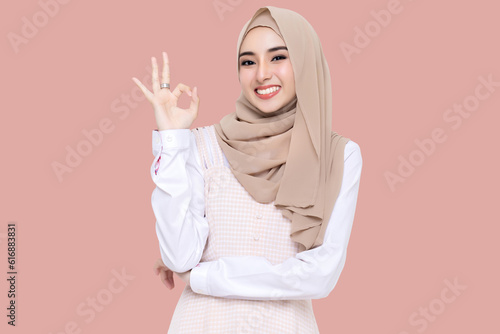Beauty Asian young muslim girl wear hijab headscarf smiling and making OK hand sign isolated on pink background. © RedcupStudio