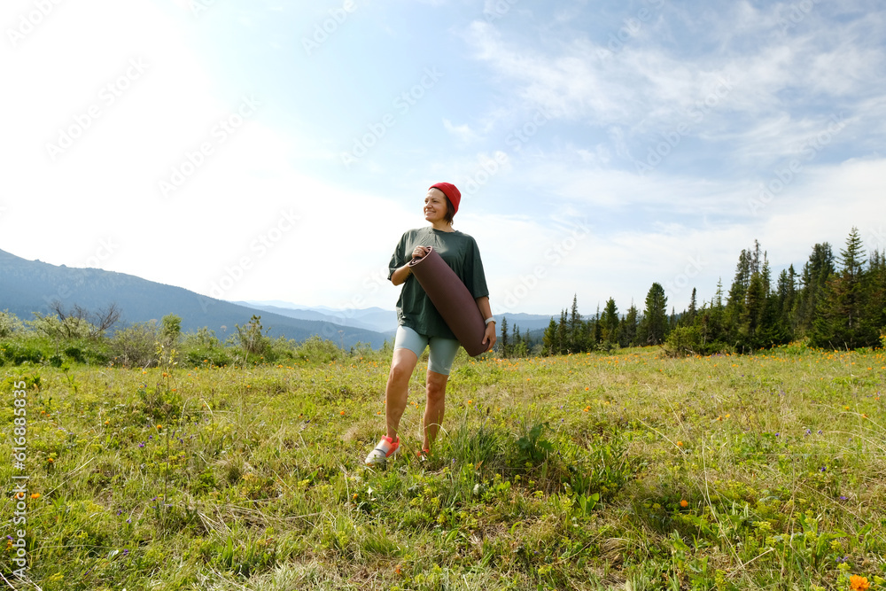 Wman doing yoga on blossom meadow and mountains background. Morning healthy activity.