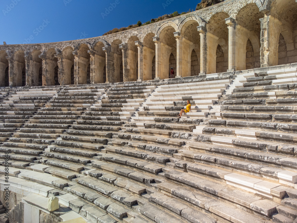 Cute woman tourist in yellow dress siting in ancient amphitheatre Aspendos 