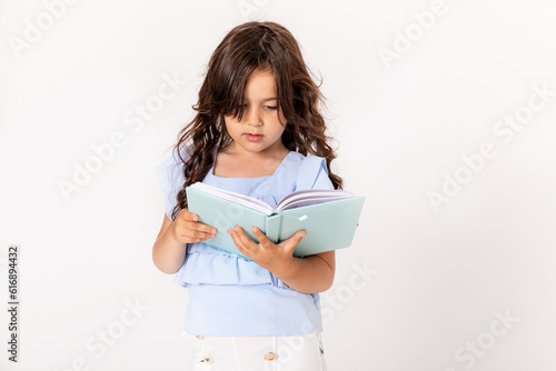 Smiling little kid girl in blue shirt onwhite background children portrait. Childhood lifestyle concept. Mock up copy space. Hold book, notebook