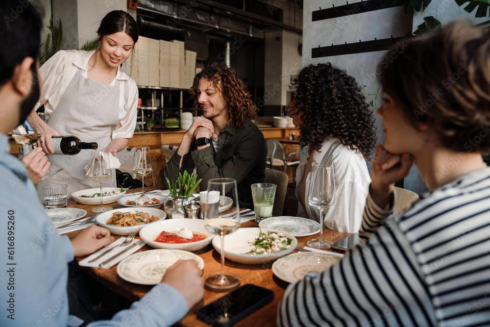 Waitress pouring wine into glasses while serving group of friends in restaurant