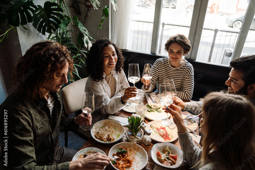 Group of multiethnic friends drinking wine while dining in restaurant