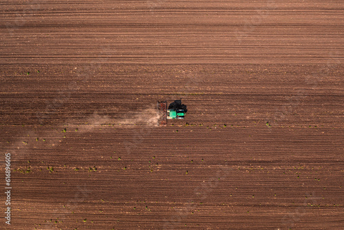 Agricultural tractor with tiller attached performing field tillage before the sowing season, aerial shot seen from the drone pov