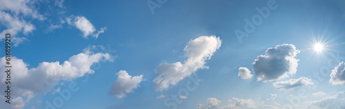 wide blue sky with bright sun and cumulus clouds