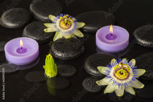 Beautiful spa concept of blooming passiflora flower  candles on zen basalt stones with drops in dark water