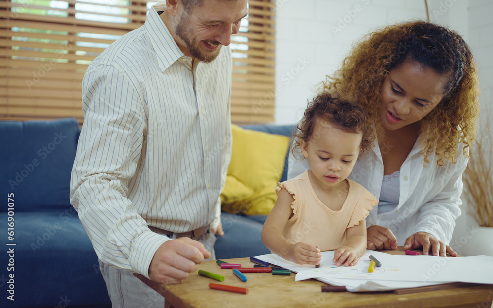Dad, Mom and little daughter drawing with colorful pencils on paper happy smiling.Young family spend free time together in living room at home. Dad, Mom and little daughter drawing with colorful pencils on paper happy smiling.Young family spend free time together in living room at home.