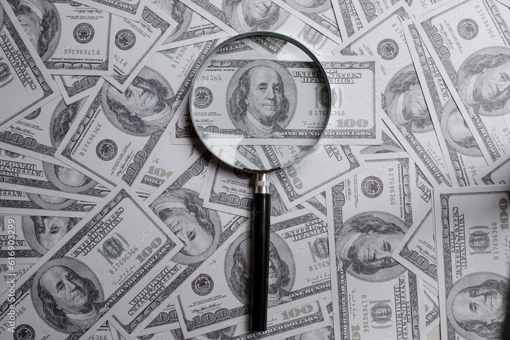 Magnifying glass on a pile of hundred us dollar money
