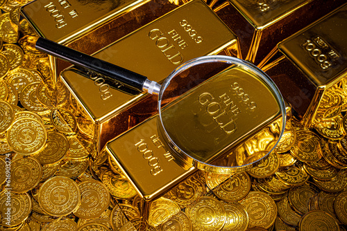 Magnifying glass with gold bar pile of gold coins under it