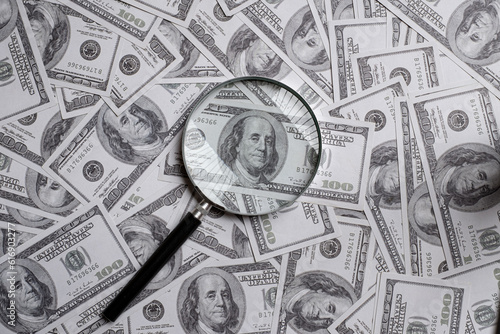 Magnifying glass on a pile of hundred us dollar money