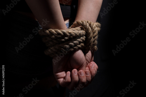 woman's hands tied with rope on black background, concept of domestic violence of the victim