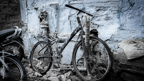 Old bicycle leaning against a blue stone wall dirty and full of paint reflecting abandonment, loneliness and sadness